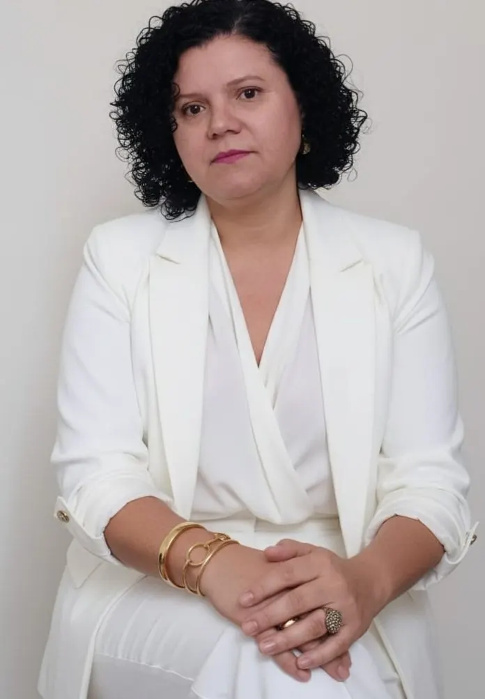 Rosemary Maria do Carmo vestida de branco, sentada, com as mãos cruzadas