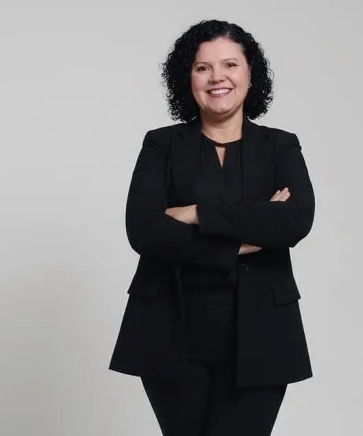 Rosemary Maria do Carmo sorrindo, de blazer preto e braços cruzados